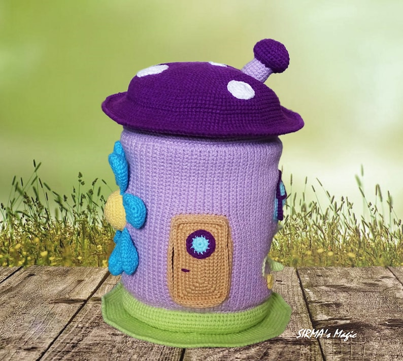 May include: A crocheted mushroom-shaped house with a purple roof, a lavender body, and a brown door with a blue peephole. The house has a green base and blue and yellow flower accents.