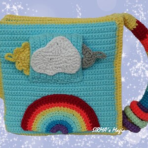 May include: A crocheted baby toy book with a rainbow, cloud, and sun design. The book has a handle and is made with colorful yarn. The text "SIRMA's Magic" is visible on the bottom right corner.