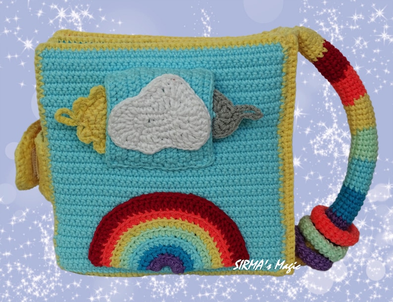 May include: A crocheted baby toy book with a rainbow, cloud, and sun design. The book has a handle and is made with colorful yarn. The text "SIRMA's Magic" is visible on the bottom right corner.