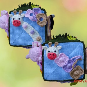 May include: Crocheted giraffe and other animal-themed decorations. The giraffe has a white face with a red mouth and is on a blue square. Other decorations include a pink elephant, flowers, and a brown purse.
