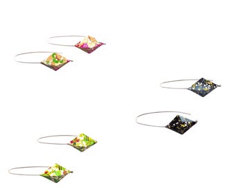 Könnte beinhalten: Eine Sammlung handgefertigter Ohrringe mit einem geometrischen, rautenförmigen Design. Die Ohrringe verfügen über verschiedene farbenfrohe Blumen- und Stoffeinsätze mit Mustern, die an dünnen, silberfarbenen Drähten befestigt sind. Die Ohrringe werden vor weißem Hintergrund präsentiert.