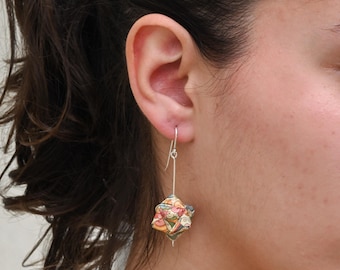 Könnte beinhalten: Ein silberner Ohrring mit einem geometrischen, mehrfarbigen Anhänger. Der Anhänger weist eine Vielzahl von Farben auf, darunter Rosa, Gelb, Grün und Blau. Der Ohrring hängt am Ohr einer Person.