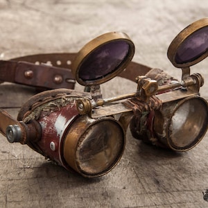 May include: Steampunk-style goggles with a brown leather strap, brass accents, and round lenses. The goggles have a distressed, vintage look.