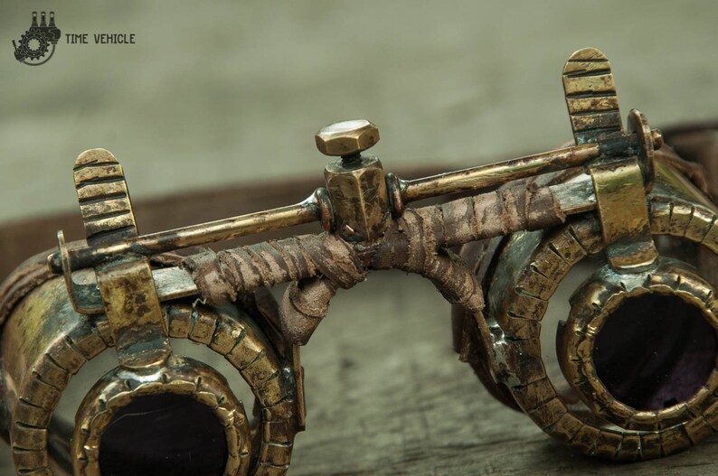 Op de afbeelding: Close-up van een steampunk-bril met messing en lederen accenten. De bril heeft ronde glazen en een leren band.