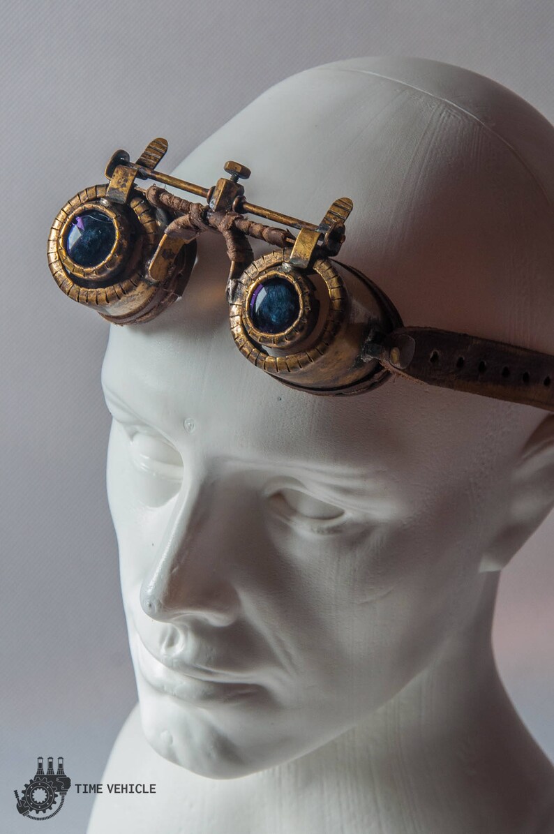 Op de afbeelding: Een paar steampunk-brillen met messing frames en blauwe glazen lenzen. De bril wordt gedragen op een wit mannequin hoofd.