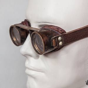 May include: Brown leather steampunk goggles with brass frames and round lenses. The goggles are worn on a white mannequin head.