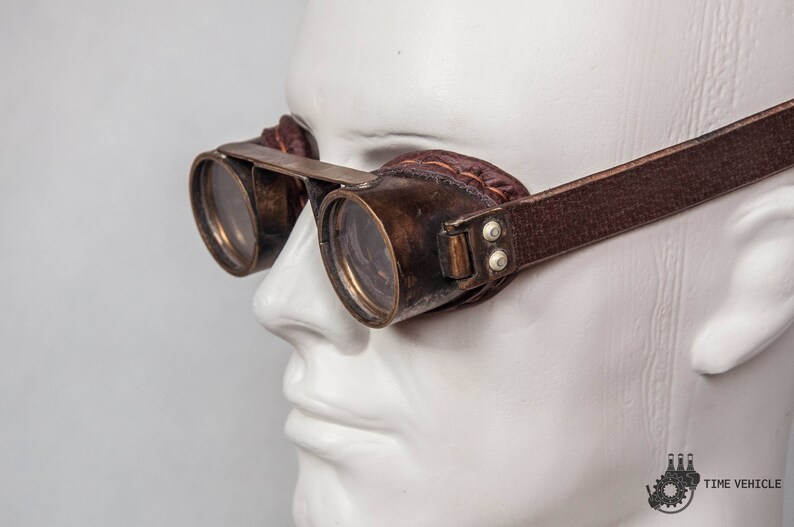 May include: Brown leather steampunk goggles with brass frames and round lenses. The goggles are worn on a white mannequin head.