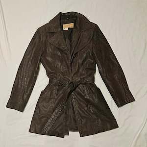 May include: A brown leather trench coat with a belt, two pockets, and a button closure. The label reads "Plus You".