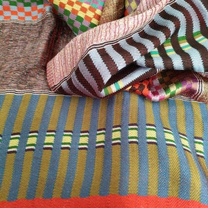 May include: A colourful woven fabric with a red, blue, green, yellow and brown striped pattern. The fabric is folded in half, showing the different patterns on both sides.