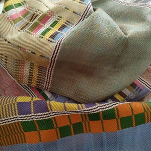 May include: A multi-colored woven fabric with a checkered pattern in shades of blue, green, orange, and purple. The fabric is folded and layered, creating a textured effect.