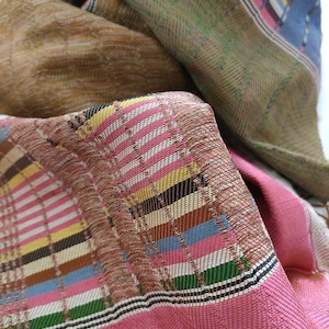 May include: A close-up of a pink, brown, green, blue and white woven fabric with a checkered pattern.