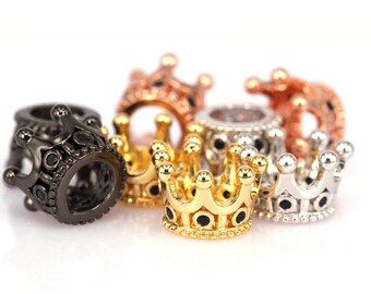 May include: A set of five crown-shaped beads in different metal finishes: black, gold, silver, and rose gold. Each bead features a black enamel center and a detailed crown design.