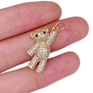 May include: Gold-tone charm featuring a teddy bear design with clear rhinestones and black eyes. The charm has a loop at the top for attaching to a necklace or bracelet.