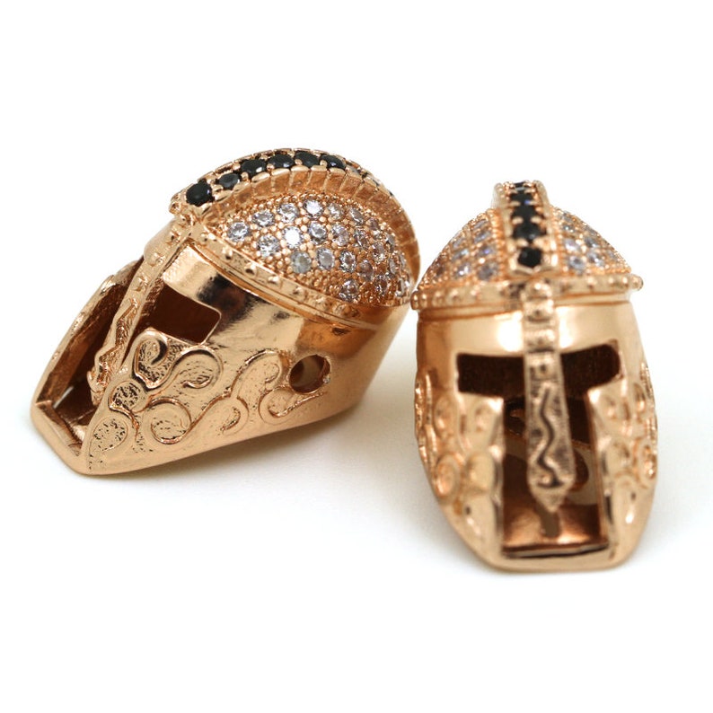 May include: Two gold-tone gladiator helmet charms with clear and black cubic zirconia stones.