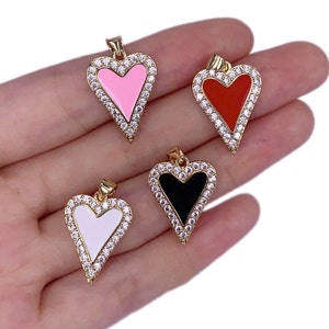Puede incluir: Cuatro colgantes de corazón de oro con un borde de diamantes de imitación transparentes. Cada colgante tiene un centro de esmalte de color diferente: rosa, rojo, negro y blanco.