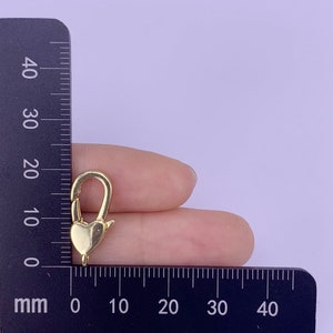 May include: Gold-toned heart-shaped lobster clasp for jewellery making. The clasp is approximately 1.5 cm long and is shown next to a ruler.