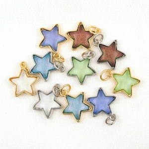 Op de afbeelding: Assortiment van tien stervormige bedels met een gouden rand en een zilveren binnenkant. Elke bedel heeft een andere iriserende kleur, waaronder blauw, groen, paars en wit.