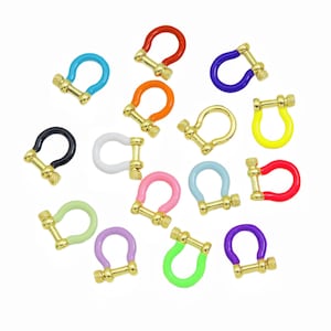 Op de afbeelding: Een verzameling U-vormige sluitingen in diverse levendige kleuren, waaronder rood, oranje, geel, groen, blauw, paars, roze, wit en zwart. Elke sluiting is voorzien van een goudkleurig metalen schroefmechanisme met een getextureerde knop.
