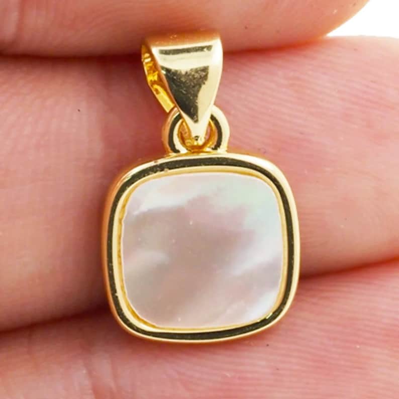 May include: A gold pendant with a square white mother of pearl inlay.