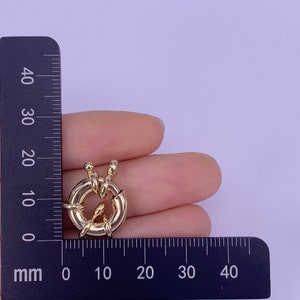May include: Gold-toned metal clasp with a circular design. The clasp is approximately 2 cm in diameter.