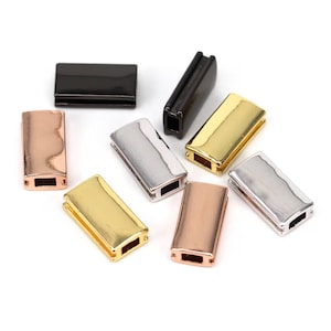 May include: Assortment of six metal slider charms in different finishes: black, silver, gold, rose gold. Each charm is rectangular with a small opening in the center.