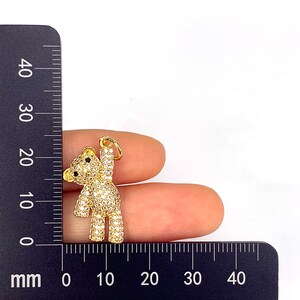 May include: Gold-tone teddy bear charm with clear cubic zirconia stones. The charm is approximately 2 cm tall.
