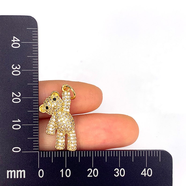 May include: Gold-tone teddy bear charm with clear cubic zirconia stones. The charm is approximately 2 cm tall.