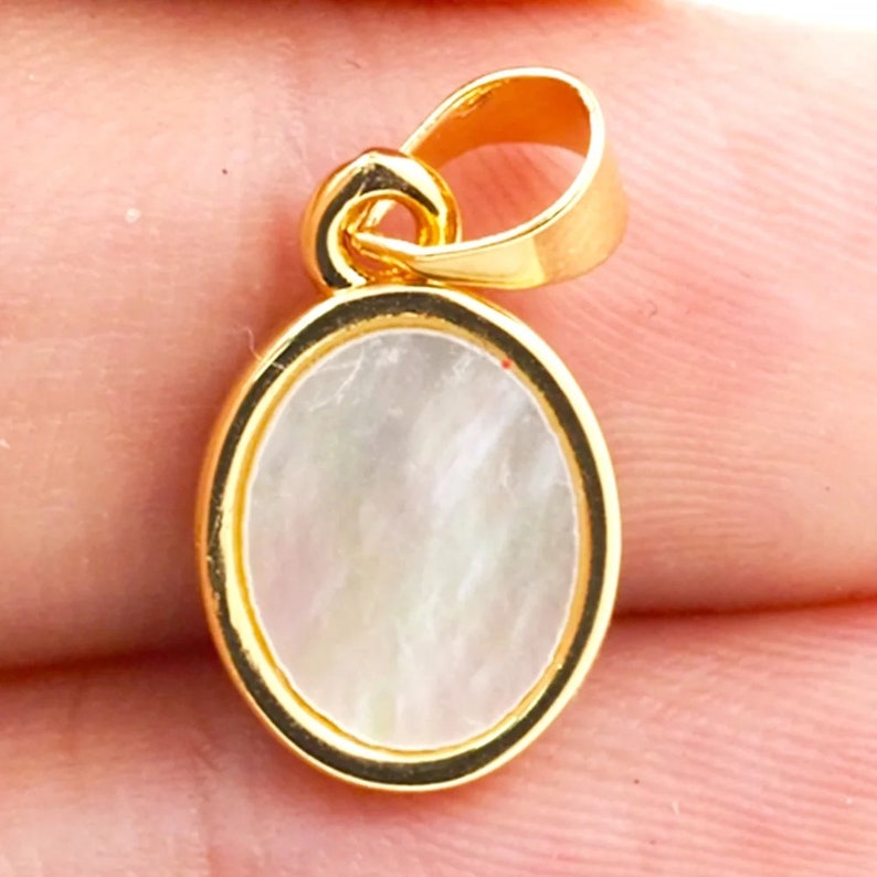 May include: A gold oval pendant with a white mother of pearl inlay. The pendant has a loop at the top for attaching to a chain.