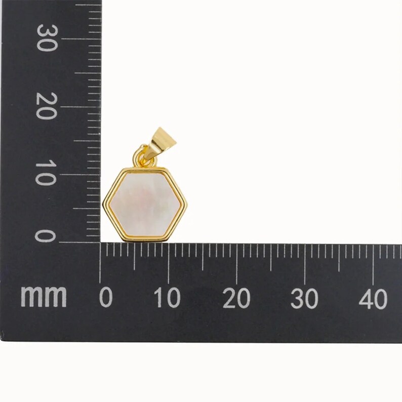 May include: A gold-toned pendant with a hexagonal white mother-of-pearl inlay. The pendant is approximately 1.5 cm wide.