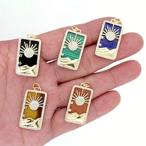 May include: Five gold-toned pendants with a sun and stars design. Each pendant features a different colored stone: black, green, brown, blue, and tiger's eye.