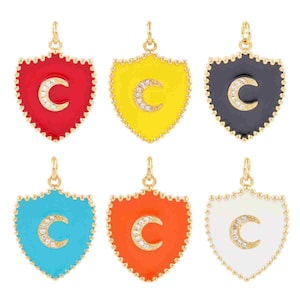May include: Six shield-shaped pendants in red, yellow, black, turquoise, orange, and white. Each pendant has a gold-colored border and a letter "C" encrusted with small, clear stones. The pendants are designed for jewelry.