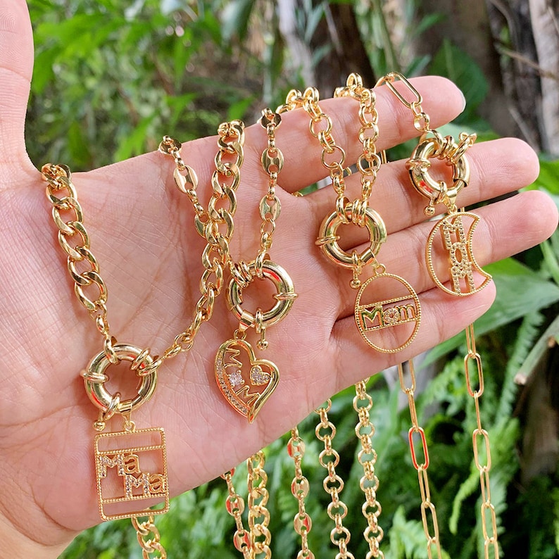 May include: Four gold chain necklaces with different charms. The charms include a heart with the word "Mama" inside, a circle with the word "Mom" inside, a crescent moon with the word "Mom" inside, and a square with the word "Mama" inside.
