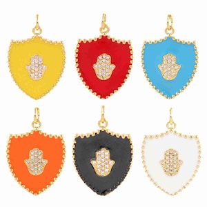 May include: Six colorful shield-shaped pendants with a gold-tone border. Each pendant features a Hamsa hand design encrusted with small, clear crystals. The pendants are in yellow, red, blue, orange, black, and white.