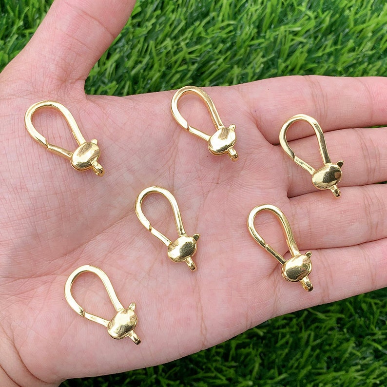 May include: Six gold-toned metal lobster claw clasps, each with a small, rounded, decorative detail at the end. The clasps are arranged in a semi-circle on a hand.