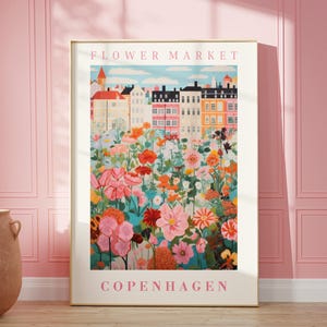Pode incluir: Uma ilustração colorida de um mercado de flores em Copenhaga. A imagem apresenta uma fileira de edifícios coloridos com um campo de flores em primeiro plano. O texto "FLOWER MARKET" e "COPENHAGEN" estão impressos em rosa na parte superior e inferior da imagem.