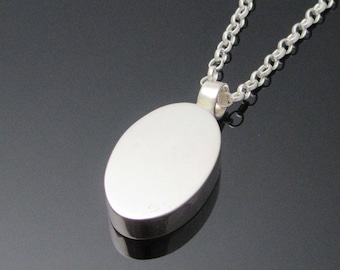 May include: A silver oval pendant necklace with a smooth, polished surface. The pendant is attached to a silver chain.