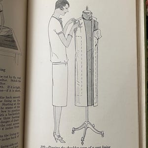Puede incluir: Un dibujo de l&iacute;nea en blanco y negro de una p&aacute;gina de libro titulada Coat-Making, p&aacute;gina 225. Representa a una persona prendiendo con alfileres la costura del hombro de un forro de abrigo en un maniqu&iacute;. El texto debajo de la ilustraci&oacute;n dice 399-Pinning the shoulder seam of a coat lining with the coat wrong side out on a dress form.