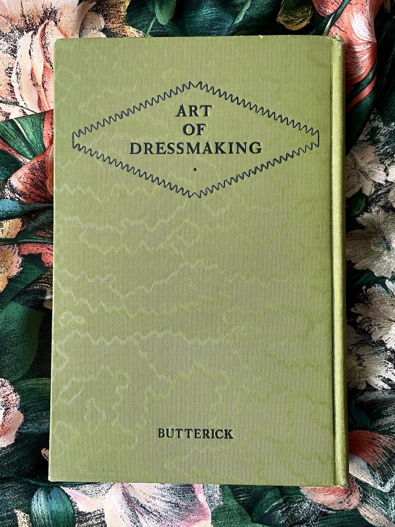 Puede incluir: Un libro de tapa dura titulado ART OF DRESSMAKING de BUTTERICK con una cubierta de color verde claro que presenta una textura acanalada vertical y un gr&aacute;fico central en forma de diamante delineado con un patr&oacute;n en zigzag. El texto est&aacute; en negro.