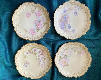 Cuatro platos de porcelana de Limoges Belle Époque pintados a mano con motivos florales, repujados, con ribete dorado y borde festoneado, de la marca Coiffe & Cie., datan de 1891-1914. Presentan rosas y pensamientos.