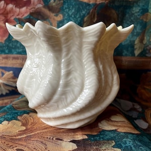 May include: A white ceramic vase with a textured, swirling design. The vase is shaped like a tulip and has a wide opening.