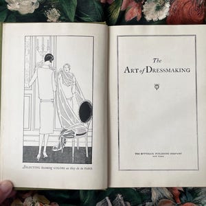 Puede incluir: Un libro antiguo abierto titulado The Art of Dressmaking de The Butterick Publishing Company New York. La p&aacute;gina izquierda presenta una ilustraci&oacute;n en blanco y negro de dos figuras con tela, subtitulada Selecting becoming COLORS as they do in PARIS.