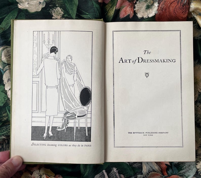 Puede incluir: Un libro antiguo abierto titulado The Art of Dressmaking de The Butterick Publishing Company New York. La p&aacute;gina izquierda presenta una ilustraci&oacute;n en blanco y negro de dos figuras con tela, subtitulada Selecting becoming COLORS as they do in PARIS.
