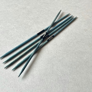 Könnte beinhalten: Ein Satz mit sechs blauen Stricknadeln mit schwarzen Spitzen. Die Nadeln sind kreuzweise angeordnet.