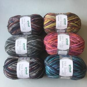 May include: Six balls of multicoloured yarn, each labelled "Hot Socks Cortina" by "gründl". The yarn features shades of brown, grey, pink, yellow, and blue. The yarn is designed for sock making and is labelled as superwash.