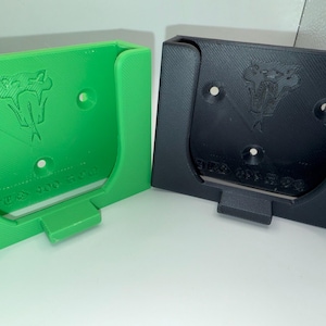 May include: Two 3D-printed wall mounts, one green and one black. Each mount features a stylized snake logo and the text "BZA 301 304". The mounts have a rectangular shape with a curved top and a small ledge at the bottom.