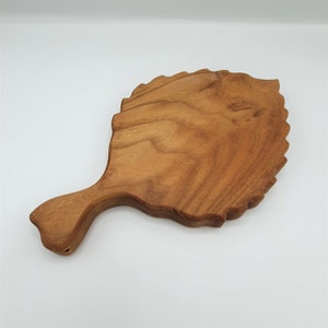 Könnte beinhalten: Ein Holzbrett in Blattform mit einem Griff. Das Brett ist aus hellem braunem Holz und hat eine natürliche Oberfläche.
