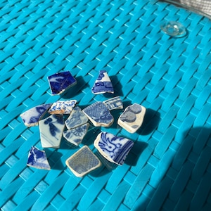 May include: A collection of blue and white porcelain shards with floral patterns. The shards are arranged on a blue woven surface.