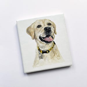 May include: A canvas painting of a golden Labrador Retriever. The dog wears a yellow and black collar with a small tag. The dog's mouth is open, revealing its pink tongue. The background is white.