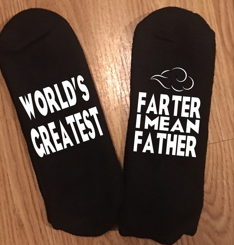 May include: Black socks with white text. One sock reads "WORLD'S GREATEST", the other reads "FARTER I MEAN FATHER" with a cloud graphic. The socks are likely a novelty gift.