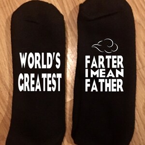 May include: Two black socks with white text. One sock reads "WORLD'S GREATEST". The other sock reads "FARTER I MEAN FATHER" with a cloud graphic above the text.